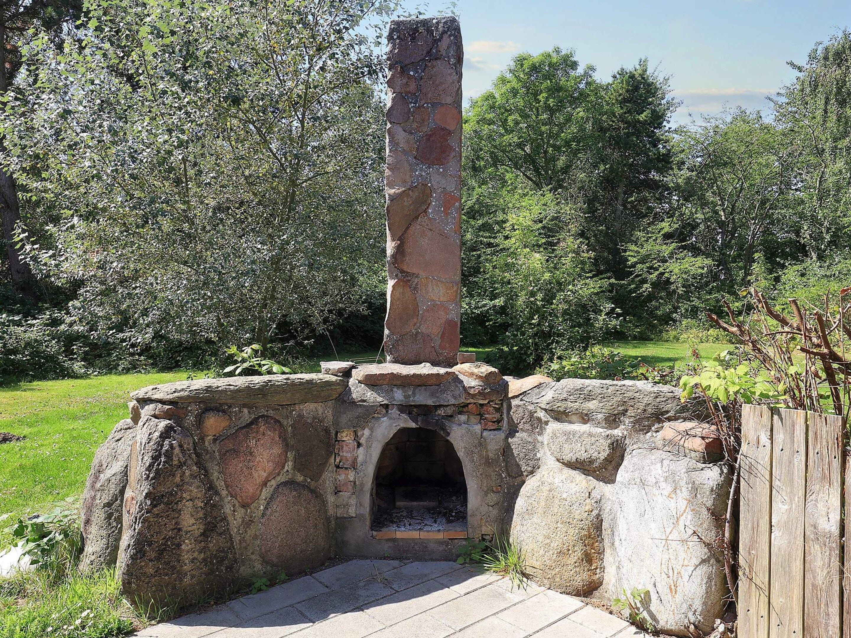 Una edificación de piedra con chimenea, rodeada de follaje.