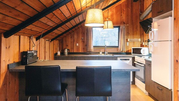 A kitchen with wooden walls, a central island with bar stools, a refrigerator, a microwave, and a stove. - 4 Star Holiday Home in Rodby (Rodby)