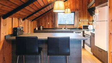 Eine Küche mit Holzwänden, einer zentralen Kochinsel mit Barhocker, einem Kühlschrank, einer Mikrowelle und einem Herd.