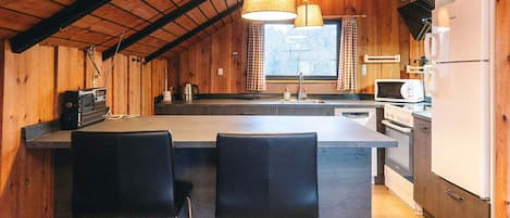 Una cocina con paredes de madera, una isla central con taburetes de bar, un refrigerador, un microondas y una estufa.