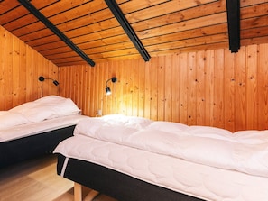 A room with two beds, wooden walls, and a sloped ceiling.