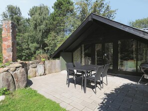 A patio with a stone wall, a wooden fence, and a table with chairs. - 4 Star Holiday Home in Rodby (Rodby)
