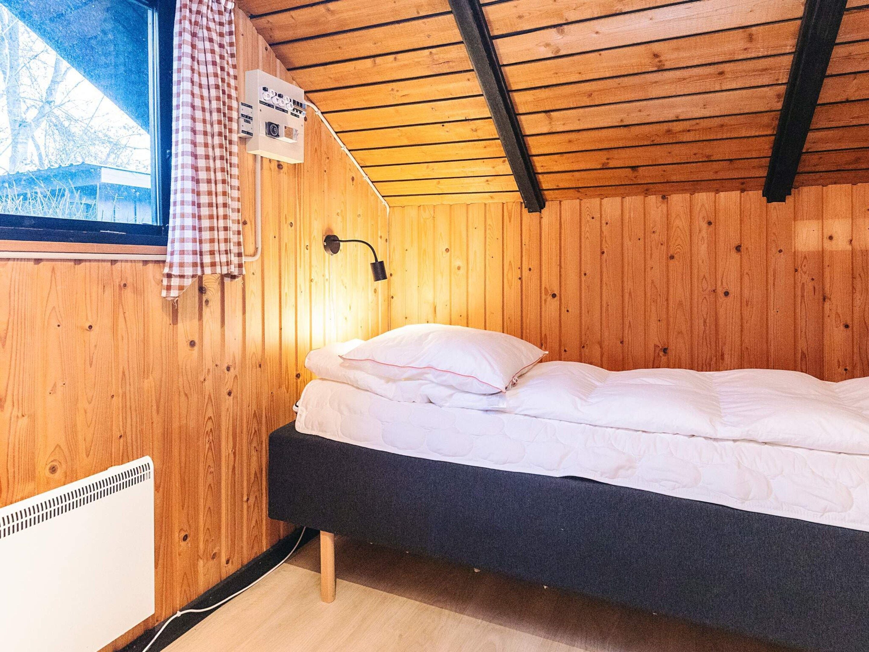 Ein Zimmer mit Holzwänden, einem Bett, einem Fenster und einem Wandheizgerät.
