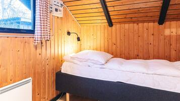 A wooden-paneled room with a bed, a window, and a wall-mounted heater.