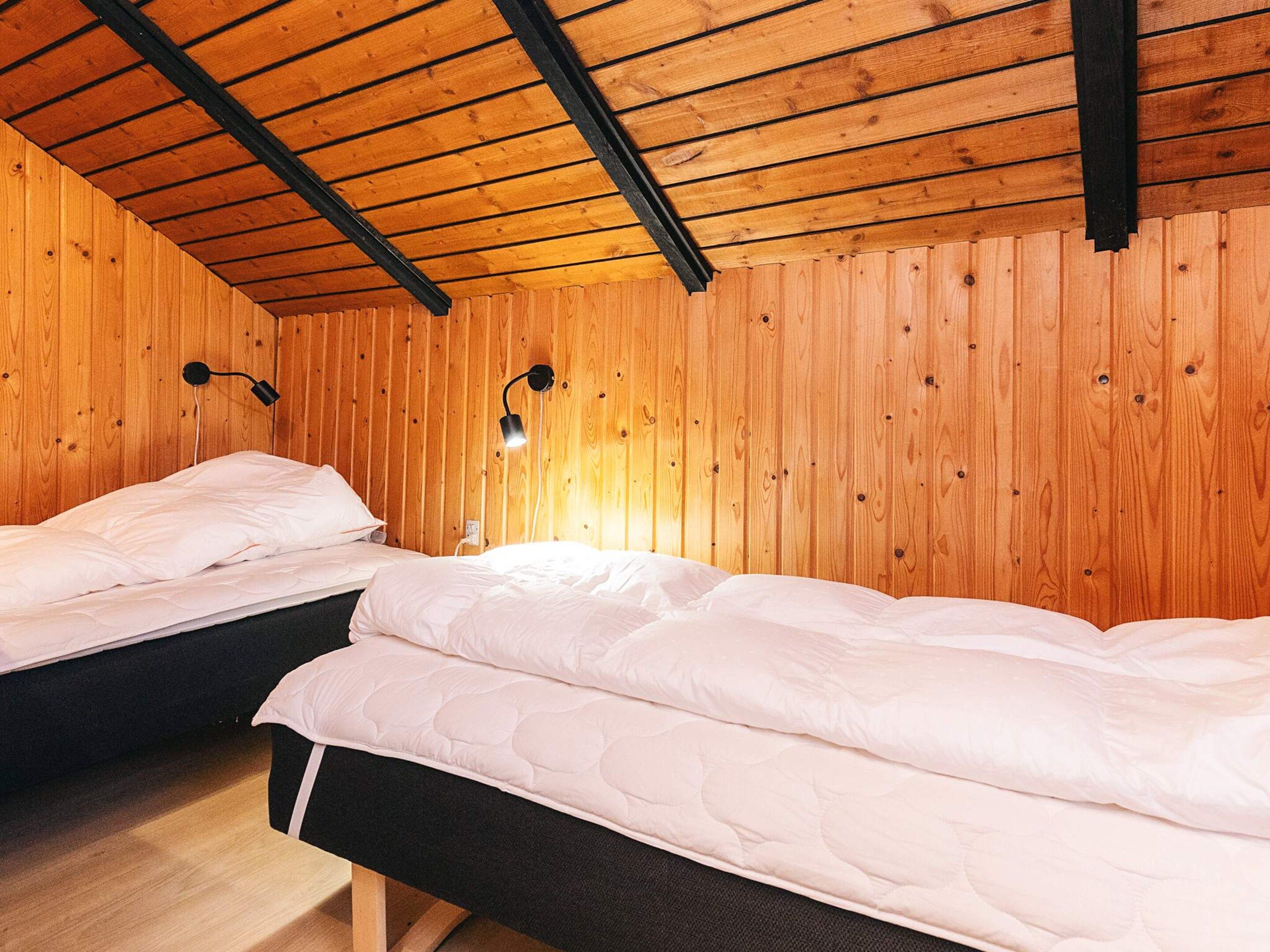 A room with two beds, wooden walls, and a sloped ceiling.
