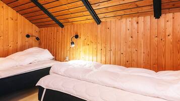 A room with two beds, wooden walls, and a sloped ceiling.