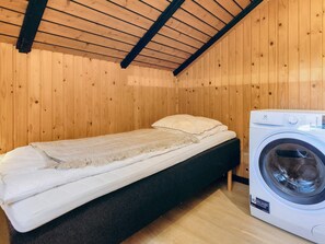 A small, single-bed room with wooden walls and a sloped ceiling. There is a washing machine to the right of the bed. - 4 Star Holiday Home in Rodby (Rodby)