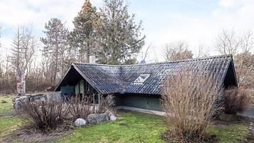 A rustic cabin with a sloped roof, surrounded by a grassy area and trees.