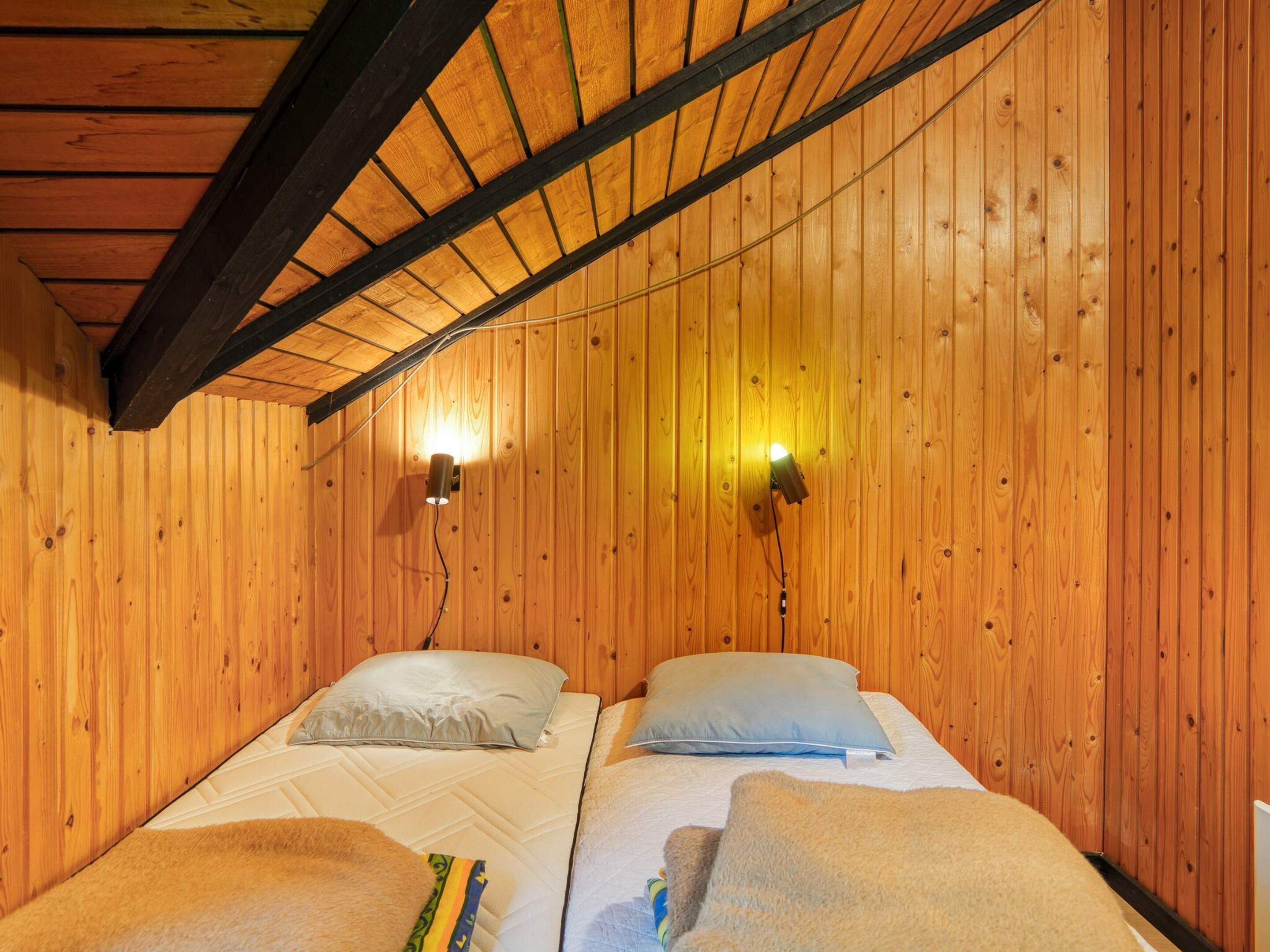 A wooden room with two beds, each with a pillow and a blanket. There are two wall-mounted lights.