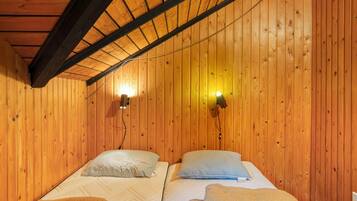 A wooden room with two beds, each with a pillow and a blanket. There are two wall-mounted lights.