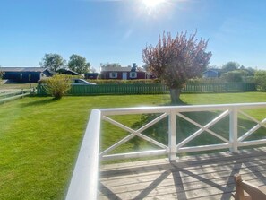 A deck with a railing overlooking a well-maintained lawn and a residential area with houses and a car. - 4 Person Holiday Home in Tvaaker (Tvaaker)