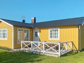Ein gelbes Gebäude mit weißer Tür, Fenstern und einer kleinen Veranda mit Geländer.