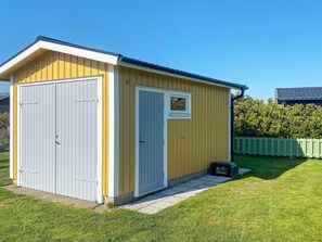 A small, single-story shed with a gabled roof, a white door, and a window. - 4 Person Holiday Home in Tvaaker (Tvaaker)