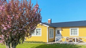 A yellow building with a white door and windows, a fenced porch, and a tree with pink flowers.