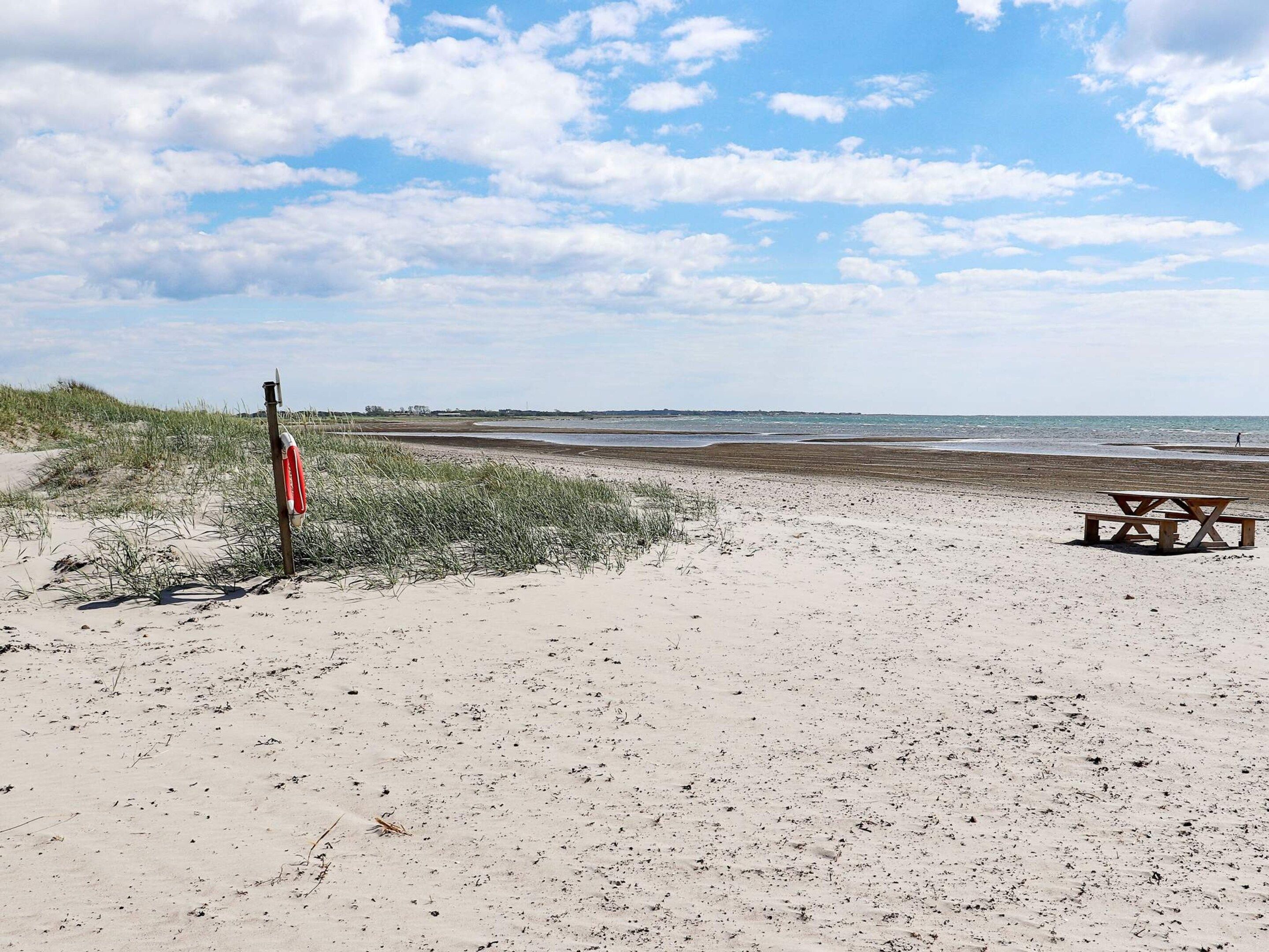 A beach with a lifeguard stand, a picnic table, and a grassy dune area.