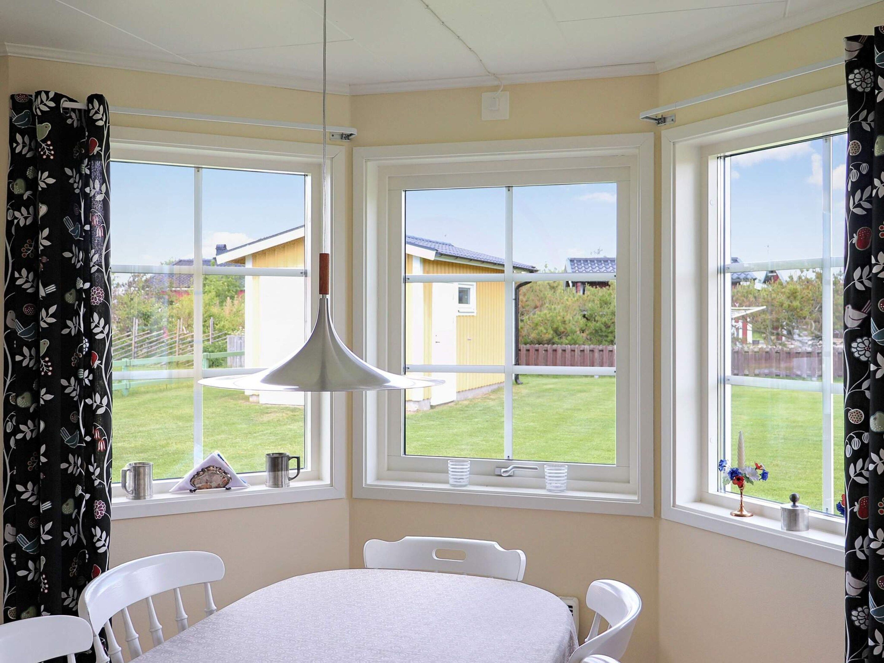 Una habitación con una mesa y sillas, ventanas grandes con cortinas y una lámpara colgante.