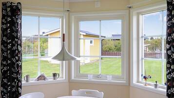Una habitación con una mesa y sillas, ventanas grandes con cortinas y una lámpara colgante.