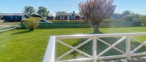 A wooden deck with a white railing, a green lawn, and houses in the background.