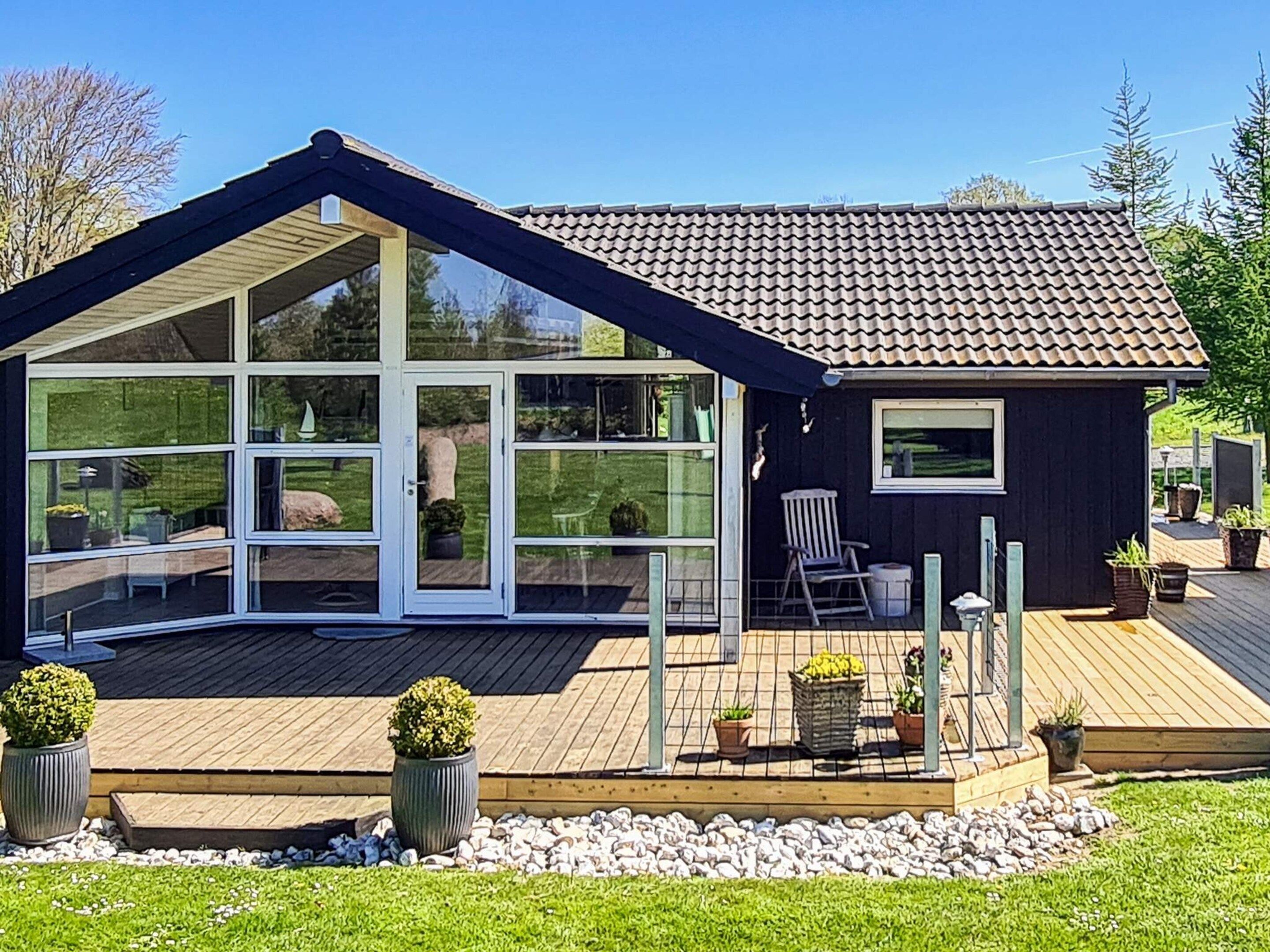 A modern house with a large glass conservatory, a wooden deck, and a small attached shed.
