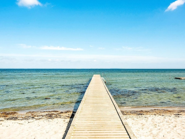 Une jetĂ©e en bois sâĂ©tendant dans une mer dâun bleu limpide, avec une plage de sable Ă son extrĂ©mitĂ©.