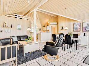 Un interior moderno con techo de madera, zona de comedor con sillas negras, sofá y pequeña cocina.