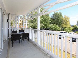 A balcony with a table and chairs, overlooking a parking area and trees. - Holiday Home in Grossenbrode (Grossenbrode)