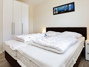 A neatly made bed with white linens, a dark headboard, and a nightstand with a lamp. - Holiday Home in Grossenbrode (Grossenbrode)