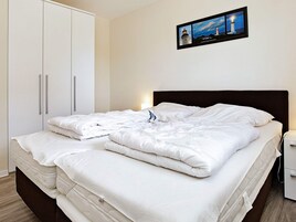 A neatly made bed with white linens, a dark headboard, and a nightstand with a lamp.