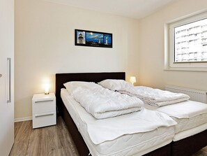 A bedroom with a bed, bedside tables, a nightstand, a window, and a framed picture on the wall. - Holiday Home in Grossenbrode (Grossenbrode)