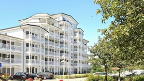 Ett hotell med flera våningar, balkonger, en asfalterad uppfart och parkerade bilar.