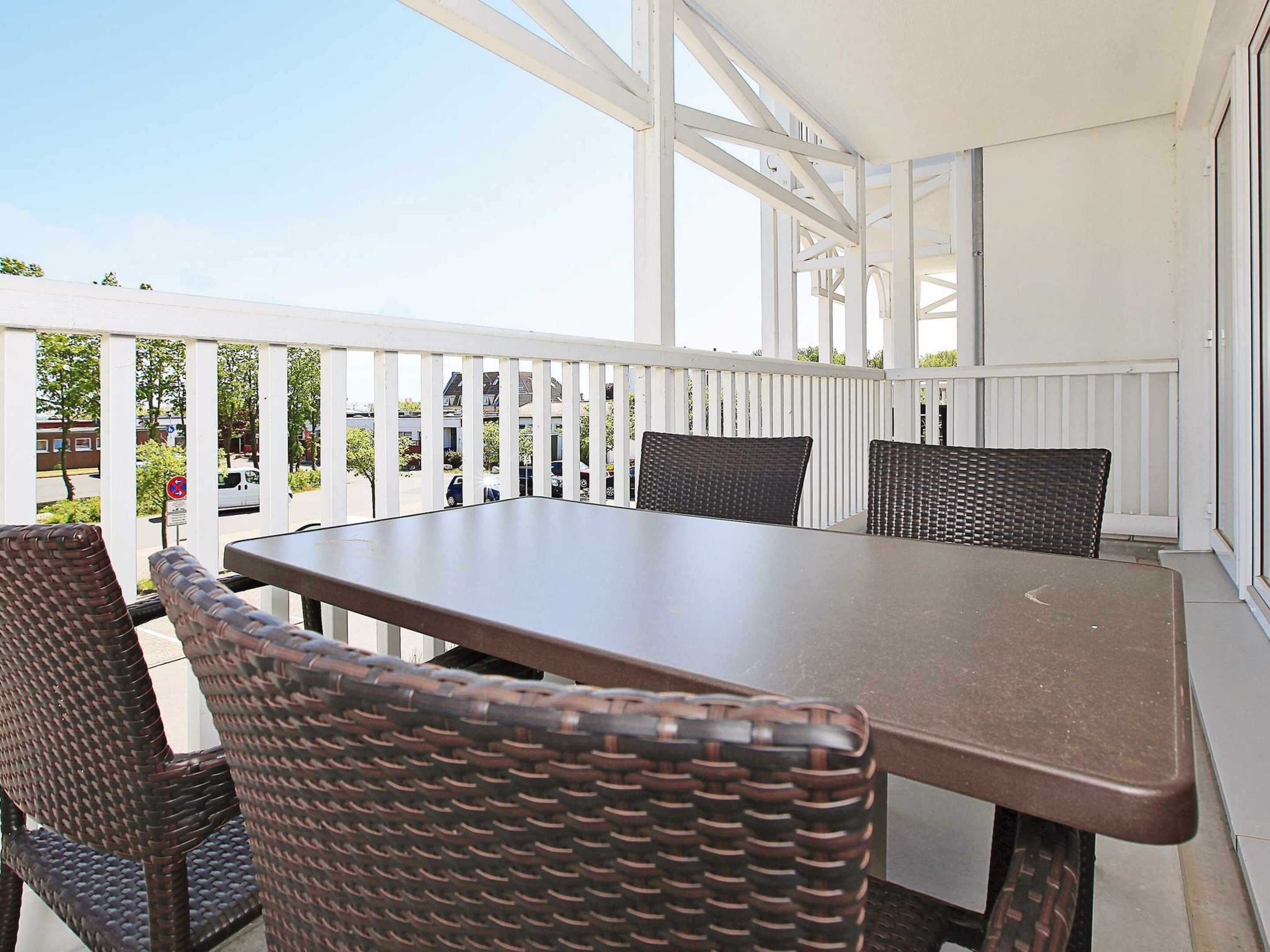 A covered outdoor patio with a table and chairs, white railings, and a view of the street.