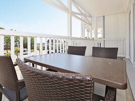 A covered outdoor patio with a table and chairs, white railings, and a view of the street.