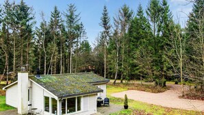 Ein kleines, eingeschossiges Haus mit schrägem Dach, umgeben von dichtem Wald.