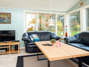 A living room with a black leather sofa, a wooden coffee table, a television, and a large window with a view of trees and a lamp. - 4 Person Holiday Home in Ans By (Ans)