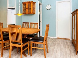 A dining area with a wooden table and chairs, a hanging light fixture, a clock on the wall, and a cabinet with glass doors. - 4 Person Holiday Home in Ans By (Ans)