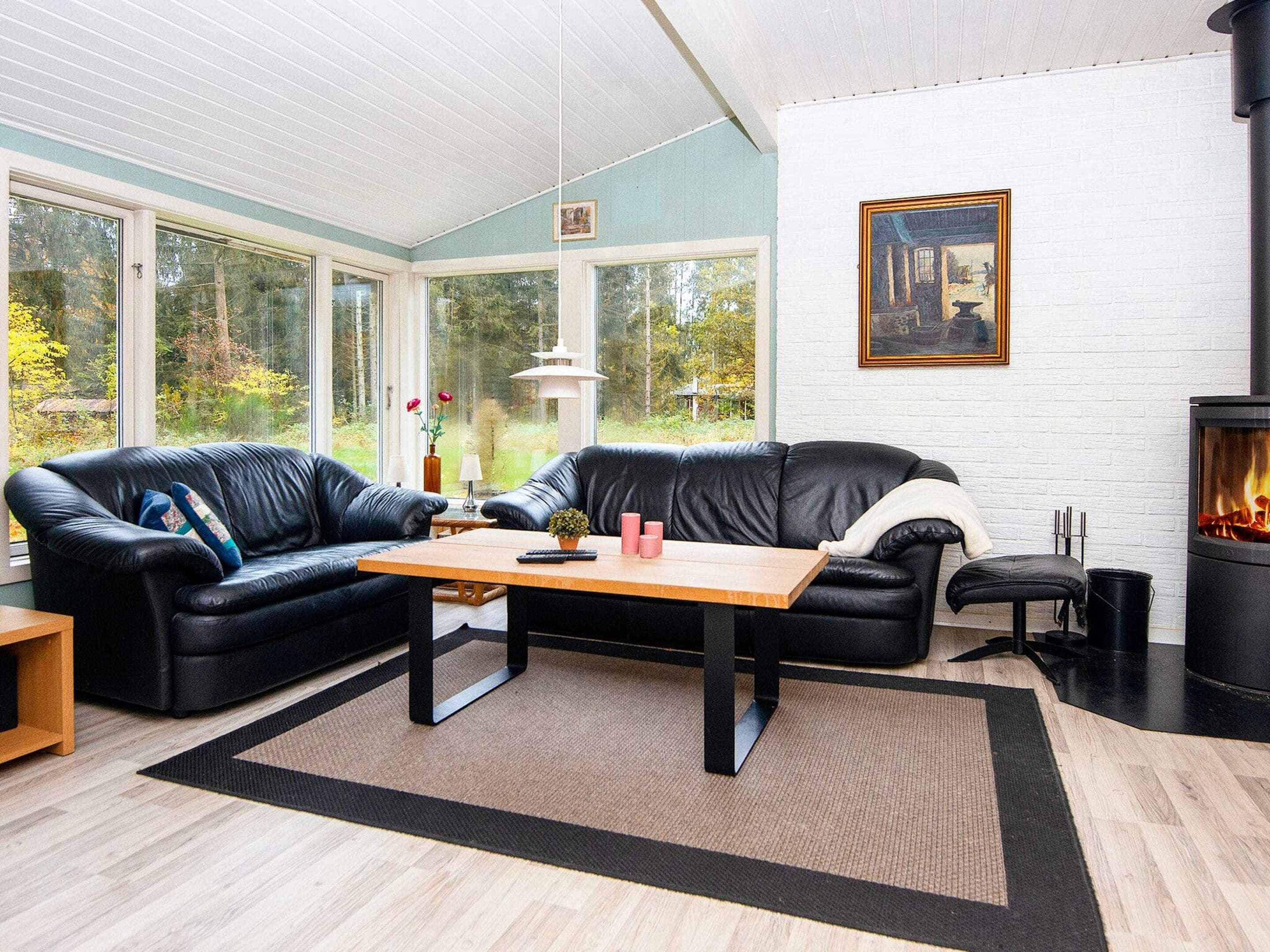 A modern living room with a fireplace, leather sofas, a coffee table, and large windows offering a view of the outdoors.