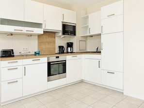 Una cocina moderna con armarios blancos, horno empotrado, microondas y cafetera.
