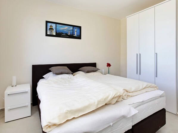 Un dormitorio con cama, mesita de noche, armario y un cuadro en la pared.