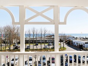 A view through a white balcony railing with a parking lot and buildings in the background. - Holiday Home in GroÃŸenbrode (Grossenbrode)