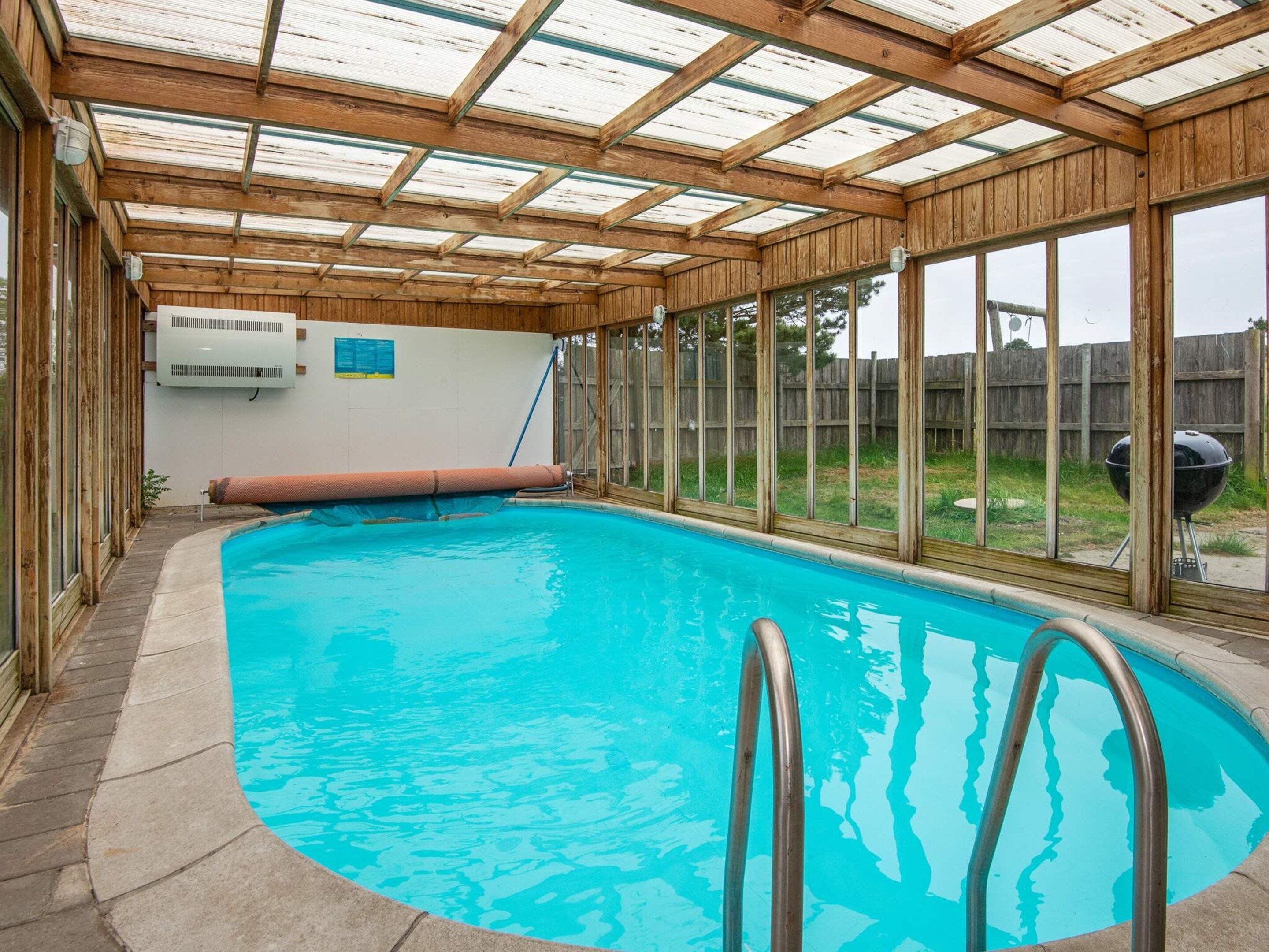 Una piscina interior con techo de madera y ventanas amplias.