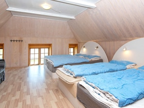 A room with two beds, wooden flooring, and a sloped ceiling.