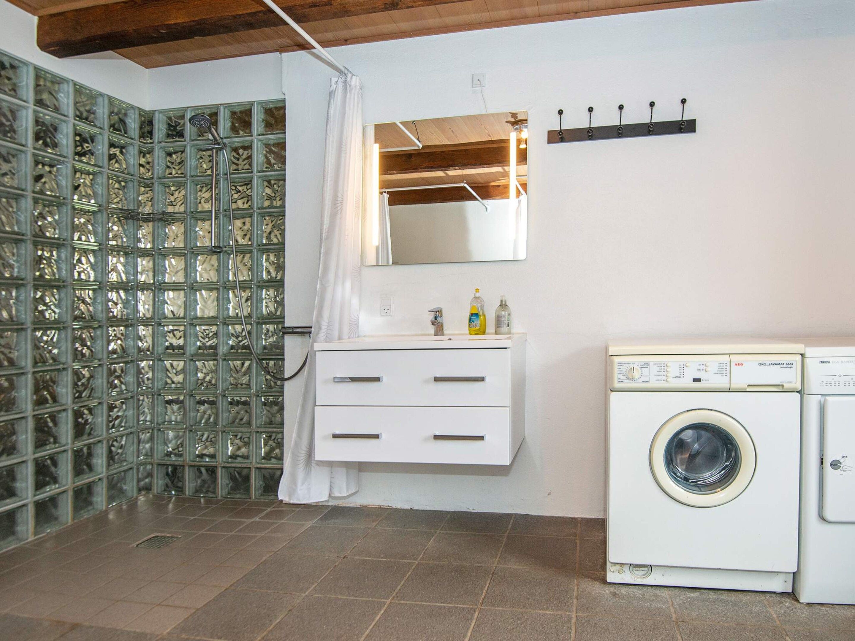A bathroom with a glass partition, a white sink with a mirror, a washing machine, and a towel rack.