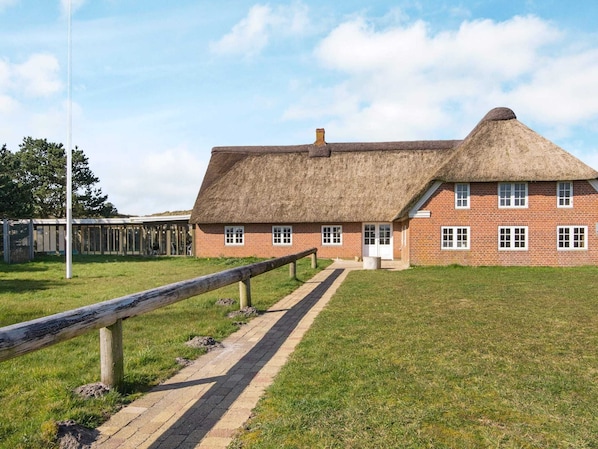 Un bâtiment traditionnel en briques, avec un toit de chaume, une clôture en bois au premier plan et un ciel dégagé.