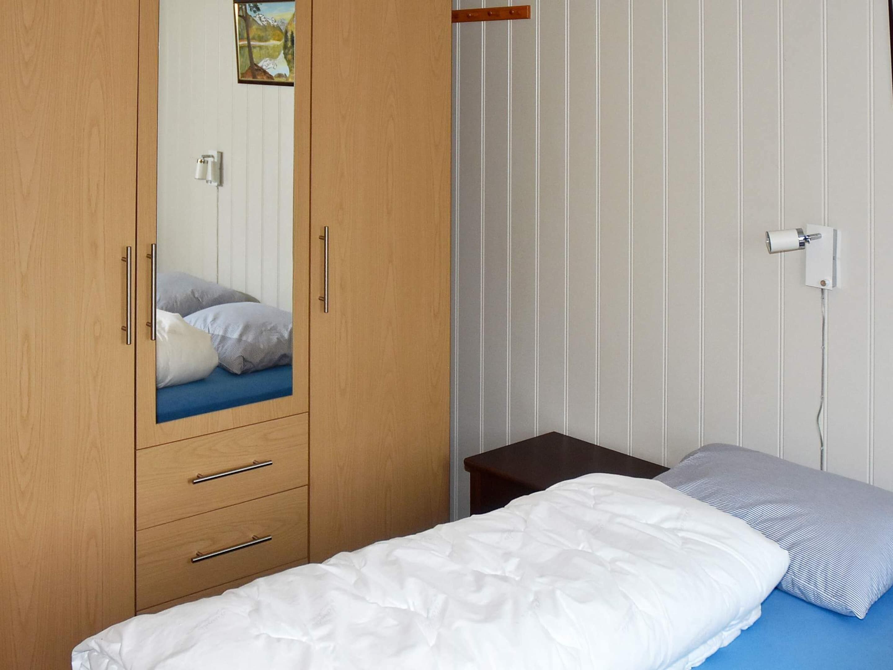 Un dormitorio con un armario de madera, una cama con ropa de cama blanca, un colchón azul y una mesita de noche pequeña.
