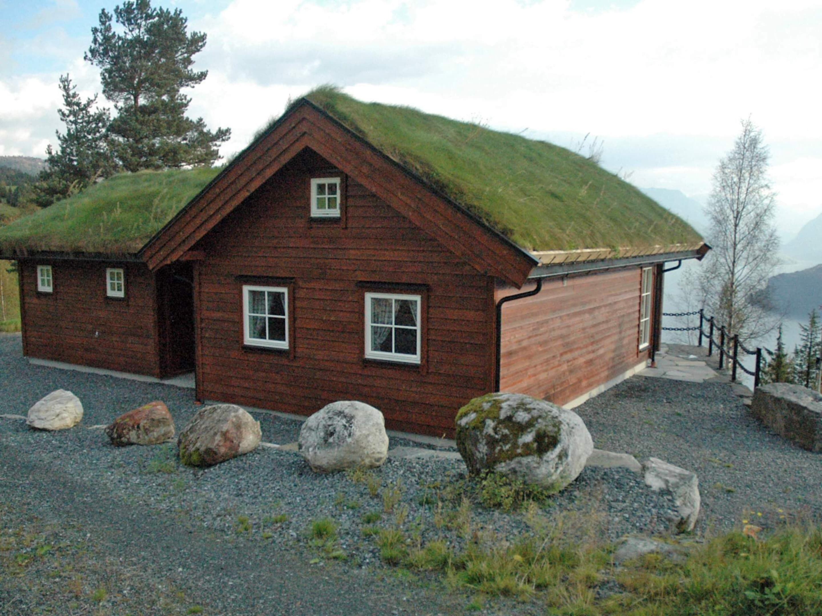A wooden house with a grass roof, a gravel driveway, and large rocks in front.