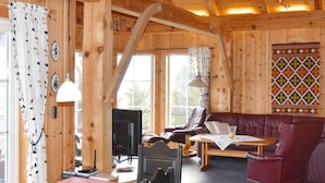 Et interiør af en træhytte med en sofa, lænestole, et bord og et fjernsyn.