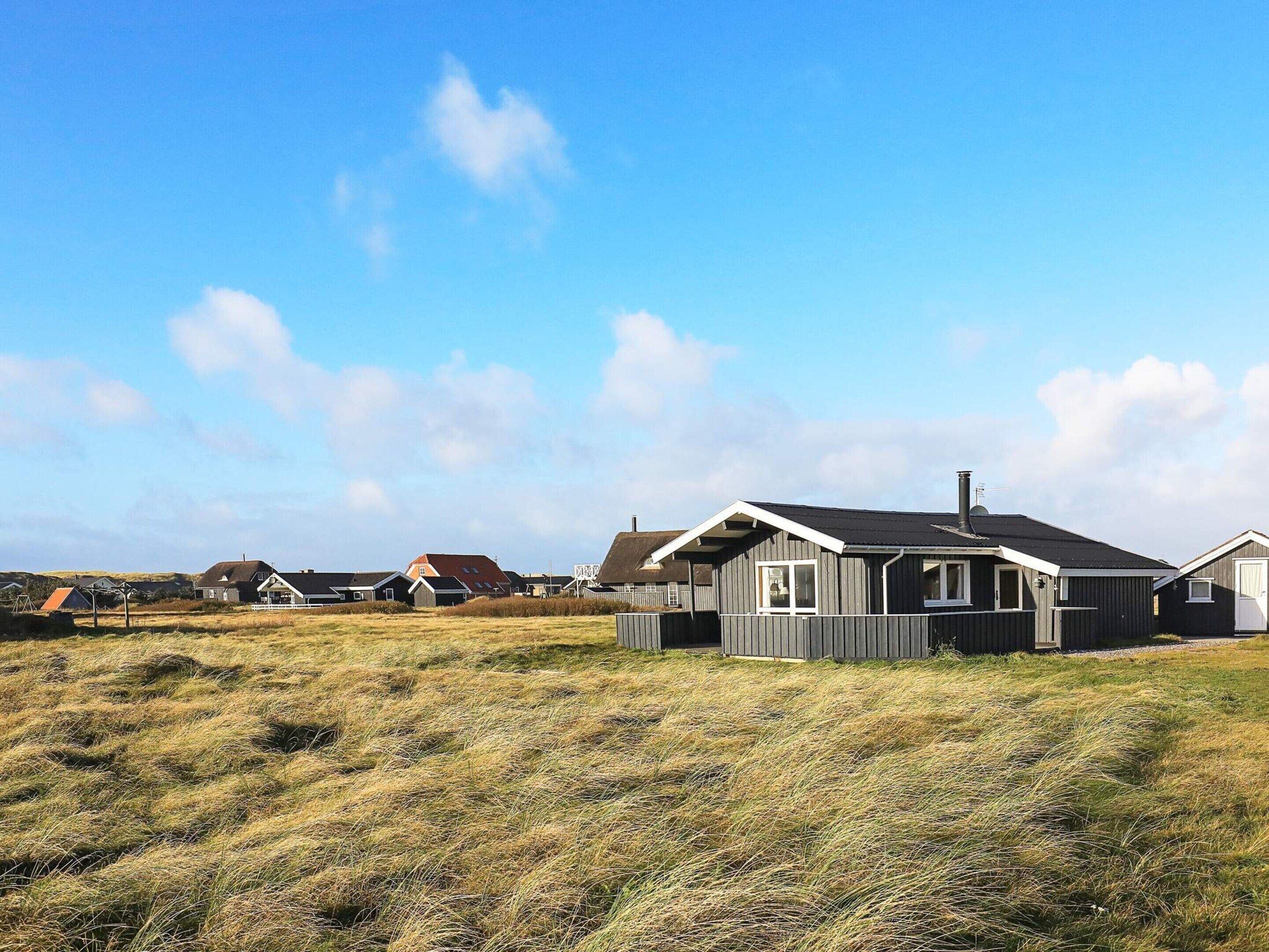 A residential area with multiple houses, a grassy field, and a clear sky.