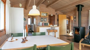 A cozy cabin interior with a dining area, kitchen, and a wood-burning stove. - 8 Person Holiday Home in Harboore (Harboore)