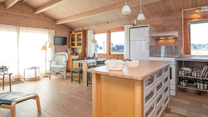 A cabin interior with a wooden ceiling, a kitchen with a built-in stove, a dining area with a table and chairs, and a seating area with a chair and a table. - 8 Person Holiday Home in Harboore (Harboore)
