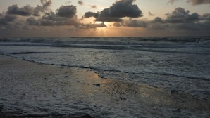 A beach with waves, a cloudy sky, and the sun setting or rising. - 8 Person Holiday Home in Harboore (Harboore)